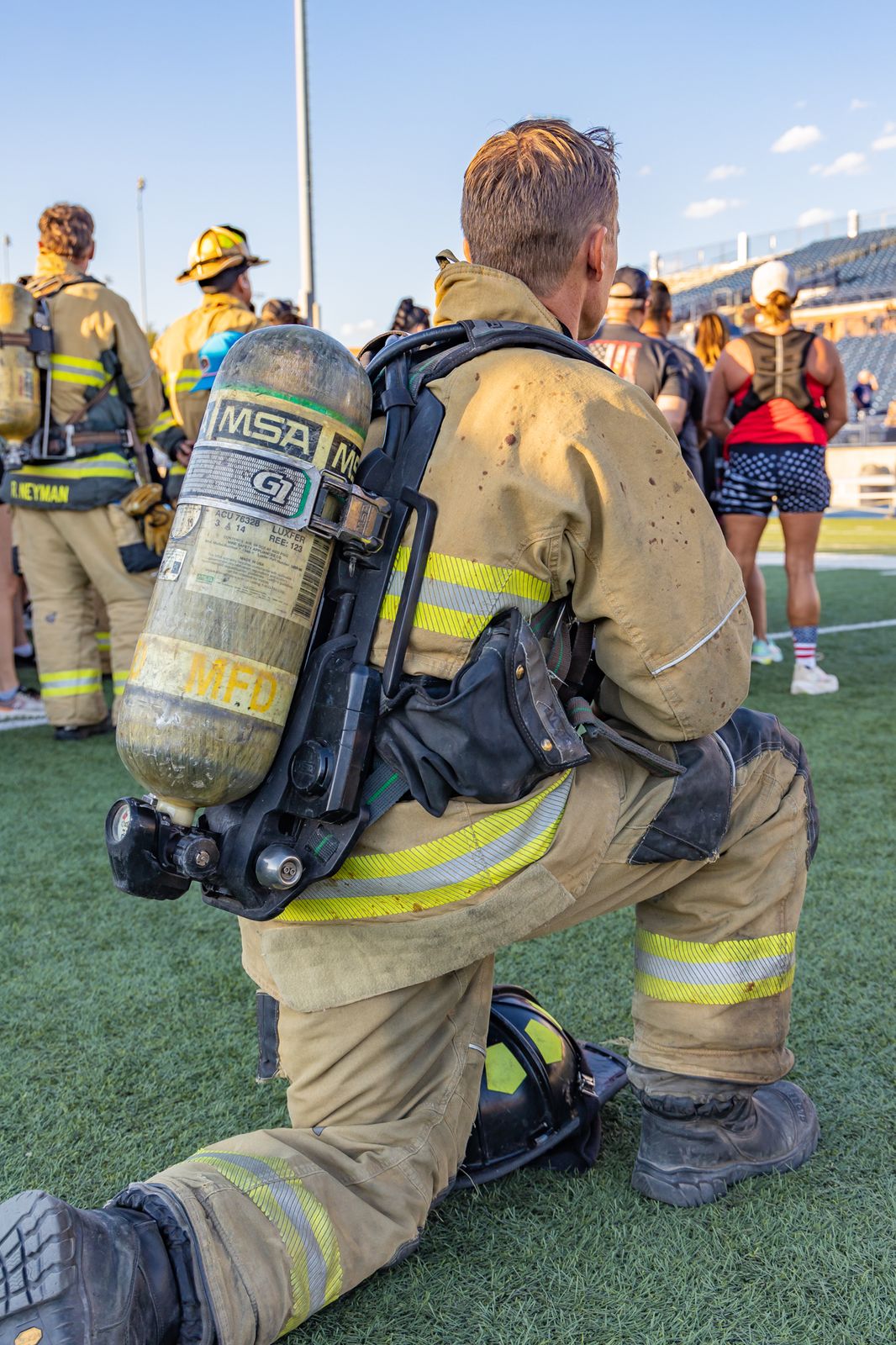 Firefighter kneeling in full gear on the stadium field before the climb
